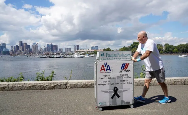 Paul Veneto pushes a beverage cart along the Boston harbor, Saturday, Aug. 21, 2021. Veneto, a former flight attendant who lost several colleagues when United Flight 175 was flown into the World Trade Center on Sept. 11, 2001, is honoring his friends on the 20th anniversary of the terrorist attacks by pushing the beverage cart from Boston to ground zero in New York. (AP Photo/Mary Schwalm)