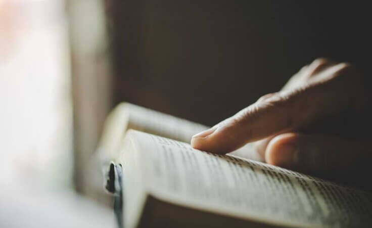 An index finger tracks along while reading an open Bible. © By doidam10/stock.adobe.com