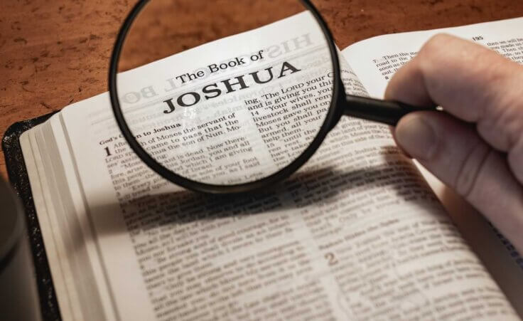 A magnifying glass highlights the title "The Book of Joshua" in an open Bible. By Jon/stock.adobe.com.