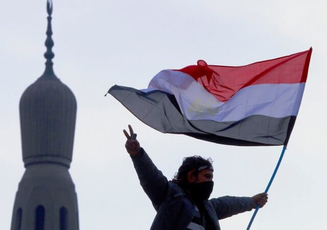 An opposition supporter flashes the victory sign as he holds an Egyptian flag atop a lamp post near a mosque in Tahrir Square in Cairo February 7, 2011. (Credit: Reuters/Yannis Behrakis)