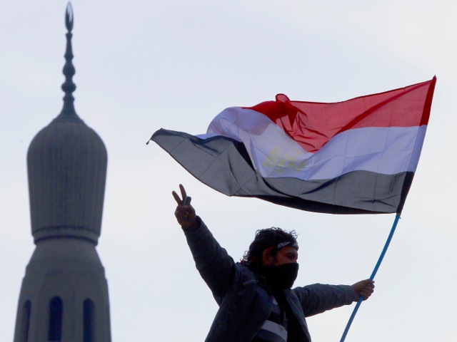 An opposition supporter flashes the victory sign as he holds an Egyptian flag atop a lamp post near a mosque in Tahrir Square in Cairo February 7, 2011. (Credit: Reuters/Yannis Behrakis)