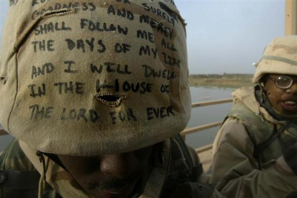 A US Army combat engineer, with Psalm 23 written on his kevlar, bows his head as he takes a short rest after securing an important two lane bridge over the Euphrates river, outside Baghdad, April 4, 2003 (Credit: Reuters/Kai Pfaffenbach)