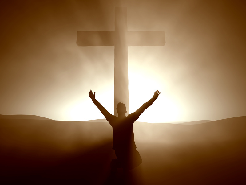A silhouette of a cross with a man kneeling arms upraised at the foot of the cross (Credit: B-C-designs via Fotolia.com)
