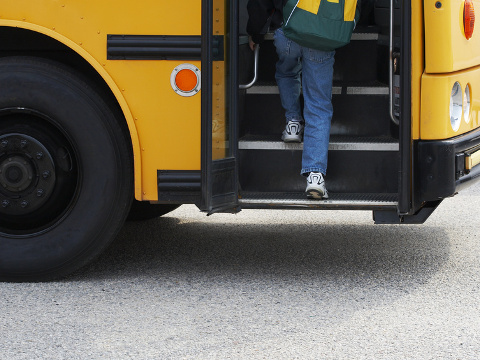 A child wearing jeans and sneakers carrying a backpack boards a yellow school bus (Credit: Glen Jones via Fotolia)