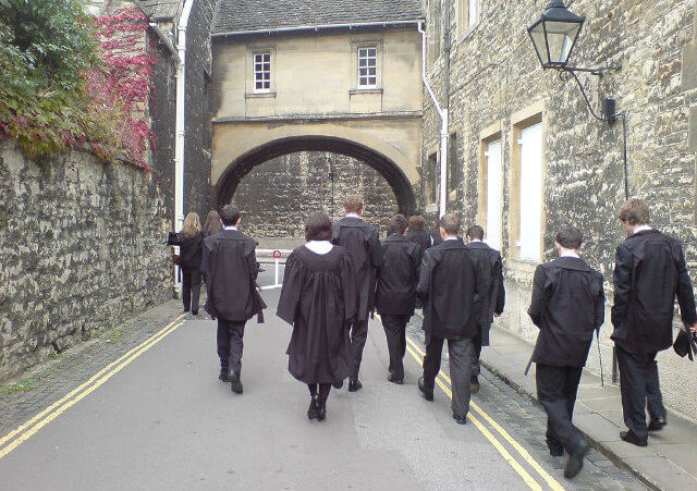 Oxford University undergraduates in academic dress walking along the eastern end of New College Lane near the entrance to New College (Credit: James via Flickr)