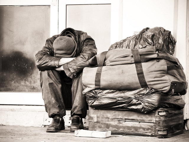 homeless man sitting on stoop head in arms with all his belongings (Credit: fmalot via Fotolia.com)