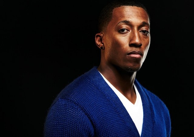 Lecrae wearing a blue football letterman sweater publicity photo for Reach Records (Credit: Reach Records)