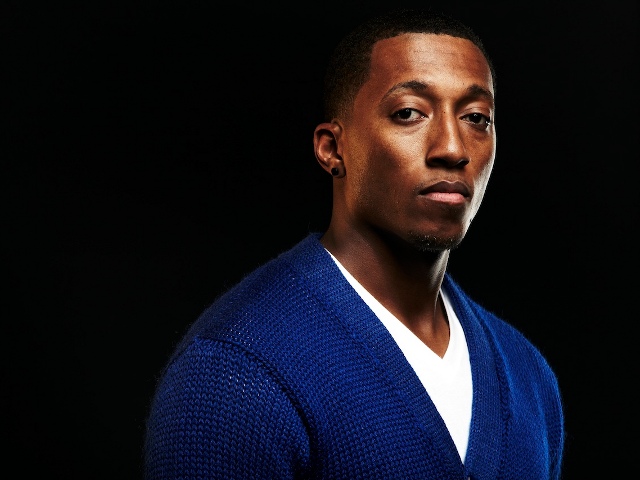 Lecrae wearing a blue football letterman sweater publicity photo for Reach Records (Credit: Reach Records)