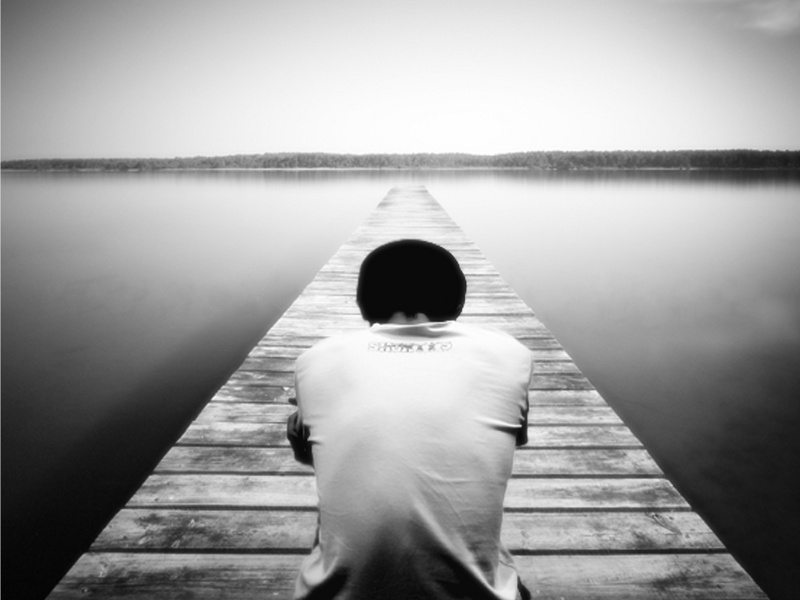 A boy sits alone on a dock that stretches into a fog shrouded lake (Credit: buaiansayapanomali via DeviantArt)