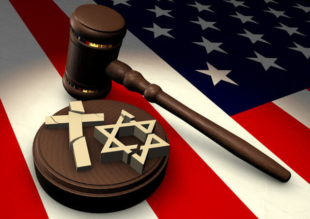 Church vs State - A gavel with a sound block that has a broken cross and Star of David on it sitting on a United States flag (Credit: James Steidl via Fotolia)