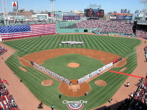 The American flag is unfurled over the Green Monster while the national anthem is sung during pregame ceremonies at Fenwary Park before the Opening Day game for the Boston Red Sox against the Baltimore Orioles, April 8, 2013 (Credit: Mike Wilkins via Flickr)