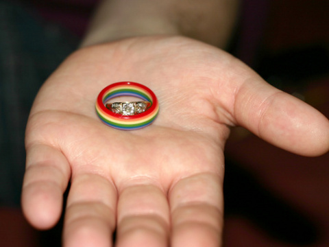 Same-sex marriage wedding ring nestled inside rainbow ring in the palm of a hand (Credit: Beth Hommel via Photos.com)
