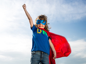 Hero Week: a young girl, with arm upraisedm standing against a blue sky, wearing a super hero costume (Credit: Igor Yaruta via Fotolia)