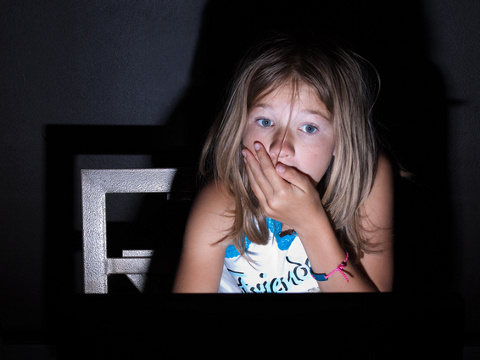 A young girl holds her hand over her mouth in shock while browsing the internet (Credit: InfinityPhoto via Fotolia)