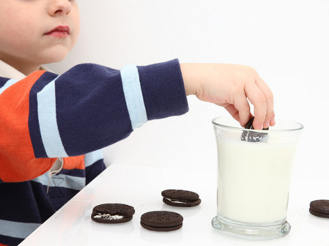 Small boy sitting at a table dipping Oreos into a glass of milk (Credit: Jaimie Duplass via Fotolia)