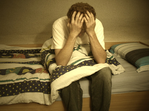 Disappointed with God, a young man sits on his bed with his head in his hands (Credit: rosental via Fotolia)