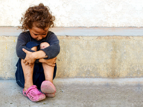 A poor, sad litle child sitting against a concrete wall (Credit: olesiabilkei via Fotolia)