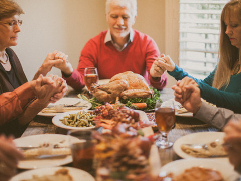 A family gathers around the Thanksgiving dinner table for prayer (Credit: Pearl via Lightstock)