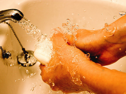 A person washing their hands in a bathroom sink with running water and a bar of soap (Credit: Lucille Pine via Flickr)