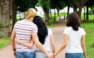 Adultery concept - a young man with his arm around one woman while holding hands with another woman, all walking down a brick path (Credit: Michael Jung via Fotolia)