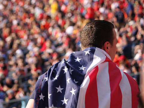 American flag draped a man's shoulders standing before a large crowd (Credit: E.N.K via Flickr)