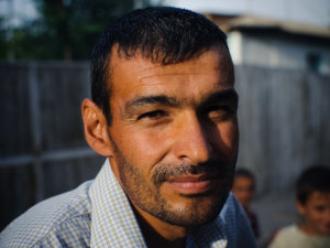 A Muslim man from somewhere in the Middle East gives a slight smile for a photo while children play in the background (Credit: Trey Hill for East-West Ministries via Flickr)