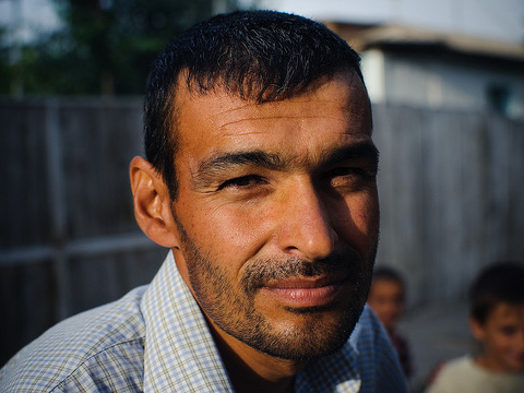 A Muslim man from somewhere in the Middle East gives a slight smile for a photo while children play in the background (Credit: Trey Hill for East-West Ministries via Flickr)