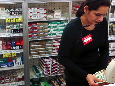 A cashier counts money in front of shelves full of cigarettes at a CVS store in the Manhattan borough of New York February 5, 2014 (Credit: Reuters/Carlo Allegri)