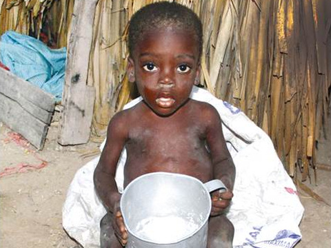 A young malnourished baby boy from Haiti named Nelson, sitting outside a home with a pot before he was rescued by Love a Child and Feed My Starving Children (Credit: Feed My Starving Children via Flickr)