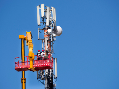 Two telecommunications workers stand in lift basket, elevated by hydraulic crane, as they perform maintenance to an antenna on a cell phone tower (Credit: fotografiche via iStockphoto)