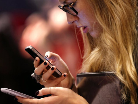 A young woman compares two smartphones, an iPhone and a Samsung Galaxy, at a trade show (Credit: Reuters/Mike Segar)