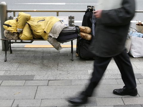 A businessman walks past a homeless man lying on a bench in Tokyo (Credit: Reuters/Yuriko Nakao)