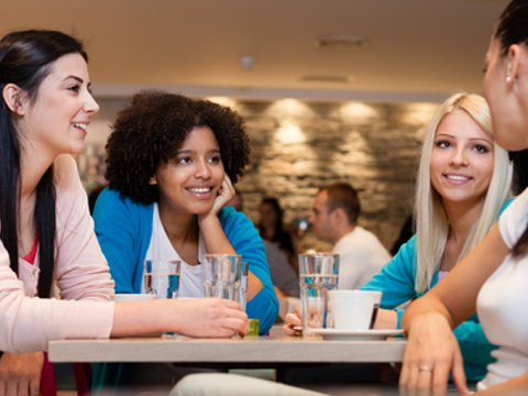 Four young women take a break and engage in conversation at a local coffee shop (Credit: Igor Mojzes via Fotolia)