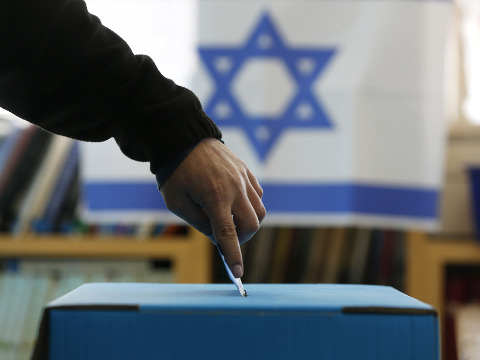 An Israeli flag is seen in the background as a man casts his ballot for the parliamentary election at a polling in the West Bank Jewish settlement of Ofra, north of Ramallah, January 22, 2013 (Credit: Reuters/Baz Ratner)