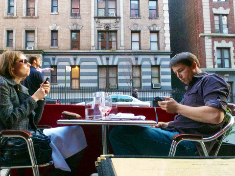 A couple, sitting at an outside table and busy on their phones, have dinner at a neighborhood restaurant in New York City, March 18, 2012 (Credit: Ed Yourdon via Flickr)