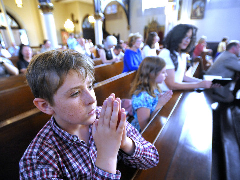 A family kneels as they pray during Mass at Saint Joseph Catholic Church in Detroit at a service that was held in response to The Satanic Temple planning to unveil its controversial goat-headed Baphomet sculpture at an undisclosed location in Detroit, July 25, 2015 (Credit: AP/Detroit News/Todd McInturf)