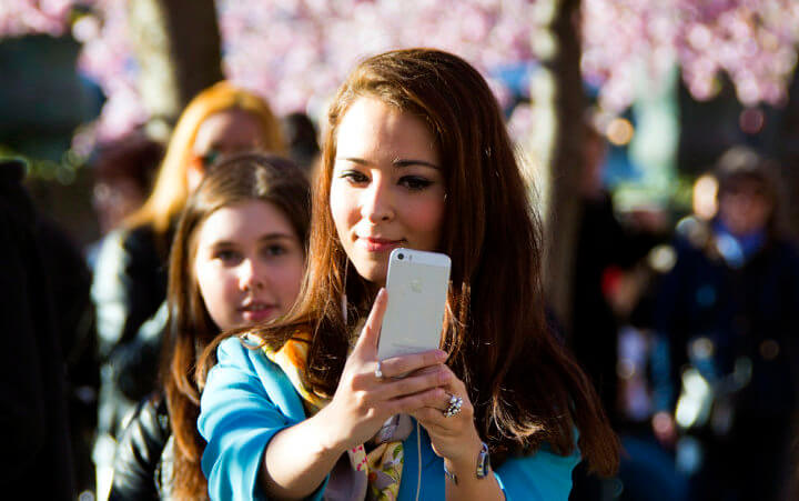 A young woman takes a selfie with friends and blossoming cherry trees in the background in the spring of 2014 in Stockholm, Sweden, April 15, 2014 (Credit: Patrik Nygren via Flickr)