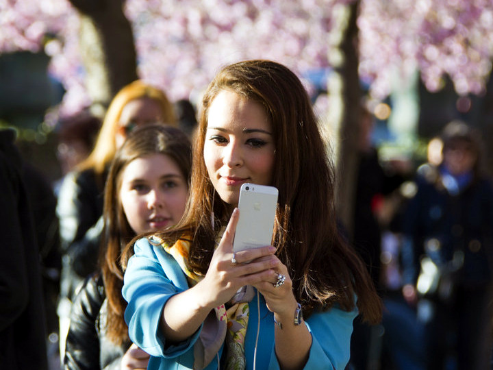 A young woman takes a selfie with friends and blossoming cherry trees in the background in the spring of 2014 in Stockholm, Sweden, April 15, 2014 (Credit: Patrik Nygren via Flickr)