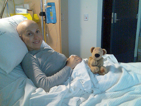 Cancer patient, Jenny Mealing, in the hospital with neutropenia, smiles from her bed with her stuffed animal (Credit: Jenny Mealing via Flickr)