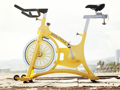 A soulcycle, a yellow stationary bike sitting outsie on a wooden dock in Santa Monica, California, August 17, 2013 (Credit: SoulCycle/@chrisfanningphoto via Instagram)
