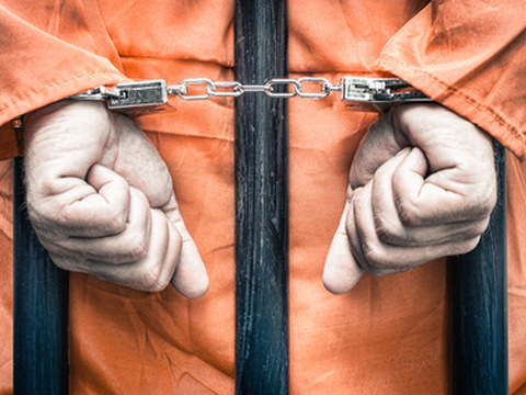 Handcuffed hands of a prisoner behind the bars of a prison (Credit: ViewApart via Fotolia)
