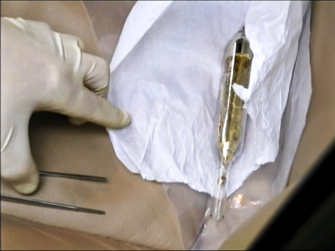 In this image made from video provided by the Moldova General Police Inspectorate, an investigator looks at a vial destined for the Islamic State containing cesium-135 on the driver's seat of Valentin Grossu's car following his arrest in Chisinau, Moldova, February 19, 2015 (Credit: Moldova Police via AP)