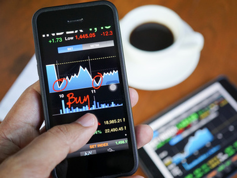 A stock market investor checking buy and sell signals on smartphone and tablet over his morning coffee (Credit: Photongpix via Fotolia)