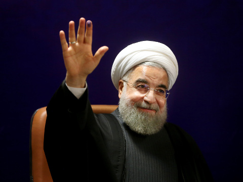 Iran's President Hassan Rouhani, who is also a member of the Experts Assembly, waves to media with an ink-stained finger, after registering his candidacy for the February 26 elections of the assembly at interior ministry in Tehran, Iran, December 21, 2015 (Credit: AP Photo/Ebrahim Noroozi)