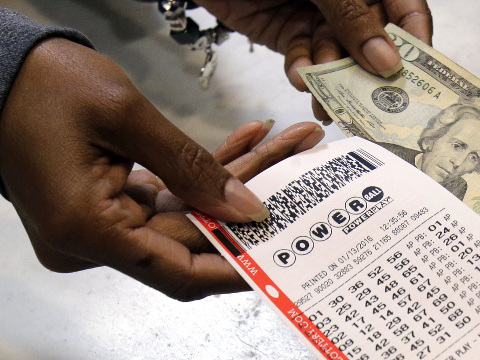 A clerk hands over a Powerball ticket for cash at Tower City Lottery Stop, Cleveland, Ohio, January 13, 2016 (Credit: AP Photo/Tony Dejak)