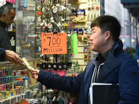 People outside a newsstand in Manhattan purchase Powerball lotto tickets. The new Powerball jackpot hit a staggering $700 million, making it the biggest in U.S. history. Powerball jackpot hits record $700 million, New York, America, January 7, 2016 (Credit: AP Images/Erik Pendzich)