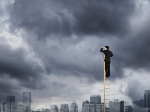 Businessman climbing on a ladder over a city looking ahead (Credit: Warakorn via fotolia)