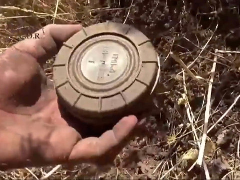 In this still image made from video taken Sept. 7, 2015 provided by the Syrian Center for Demining and Rehabilitation, a volunteer deminer takes a landmine from the ground in Daraa, Syria. Volunteer sappers in opposition-held areas of Syria are improvising their approaches to one of the world's most dangerous tasks: dismantling cluster munitions, land mines and explosive booby-traps as they work to make battle-torn areas safe for civilians to return. The result has been tragic. (Syrian Center for Demining and Rehabilitation via AP)