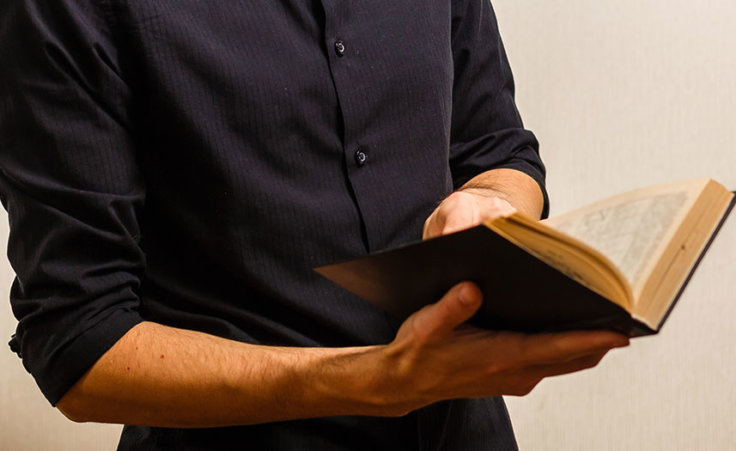 A man in a black shirt opens a Bible. Genesis 6:2 says "the sons of God saw that the daughters of man were attractive." What does this Bible passage about the sons of God and daughters of men mean?
