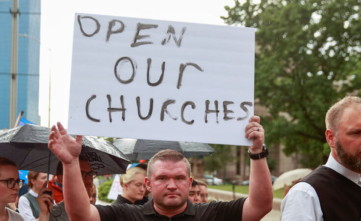A protester holds a placard that says "Open Our Churches" during the We Will Not Comply anti mask rally in Indianapolis, Indiana on July 19, 2020.